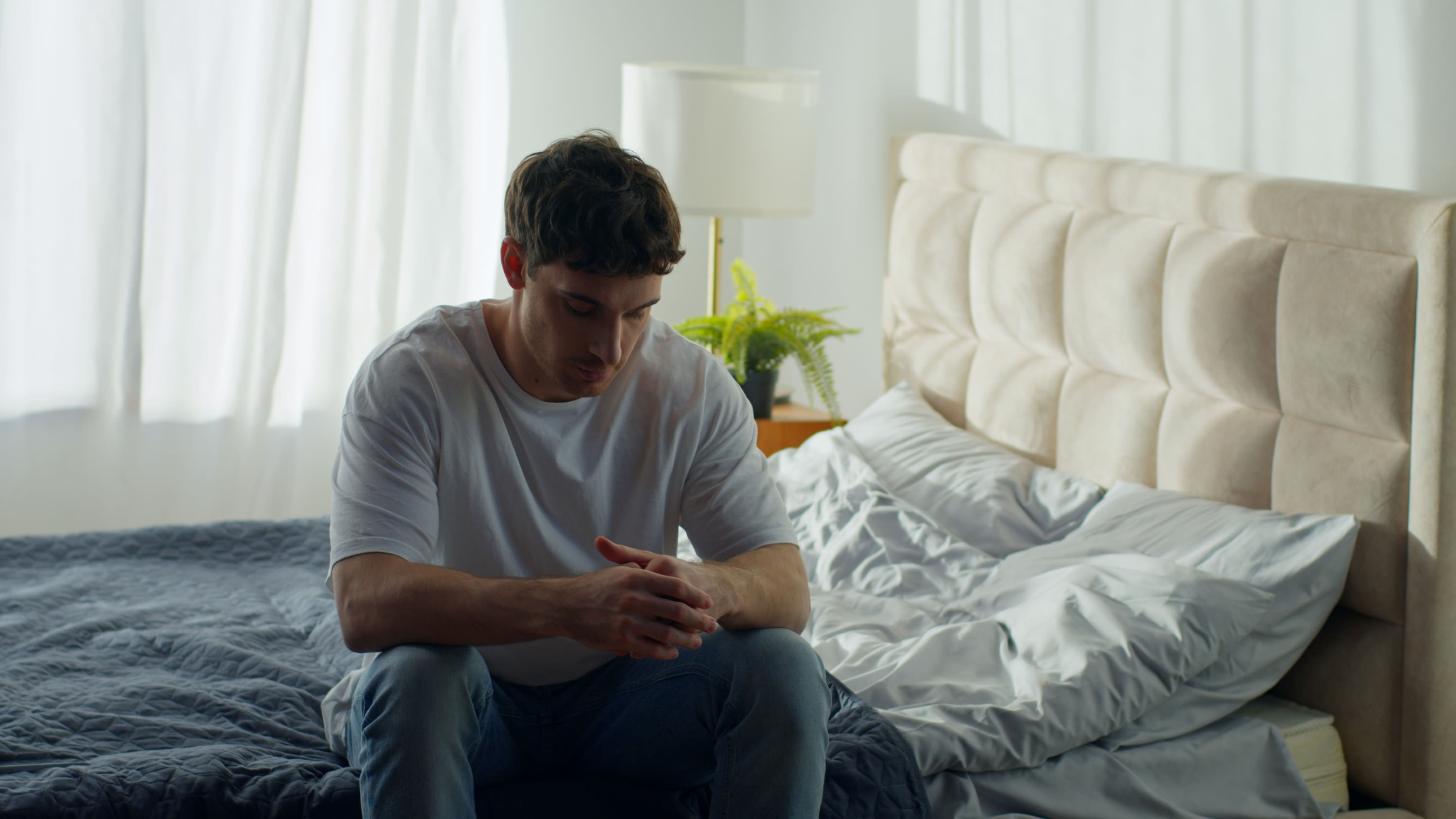 A man sitting on the edge of his bed in the morning