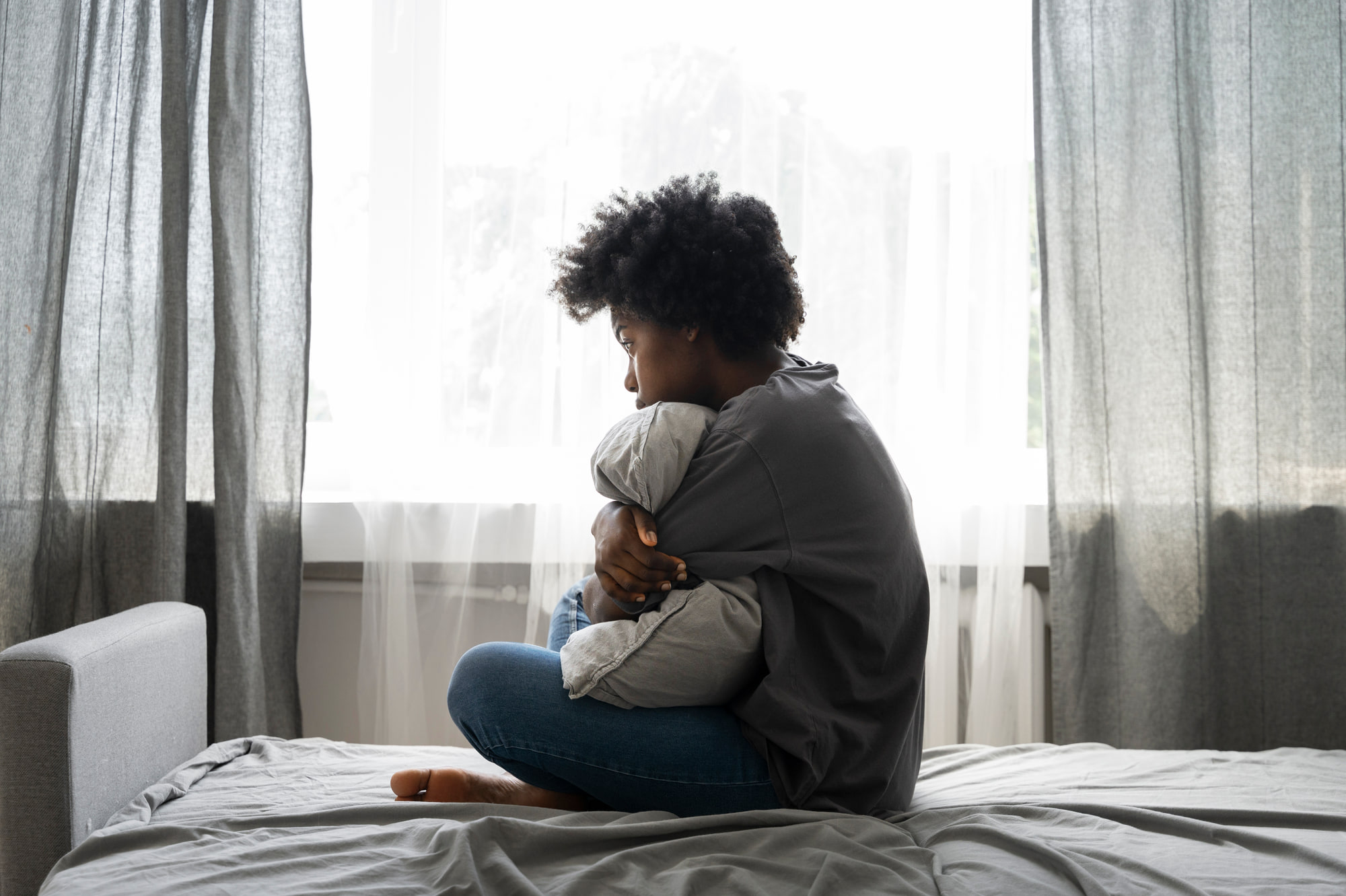 A woman sitting on her bed by the window