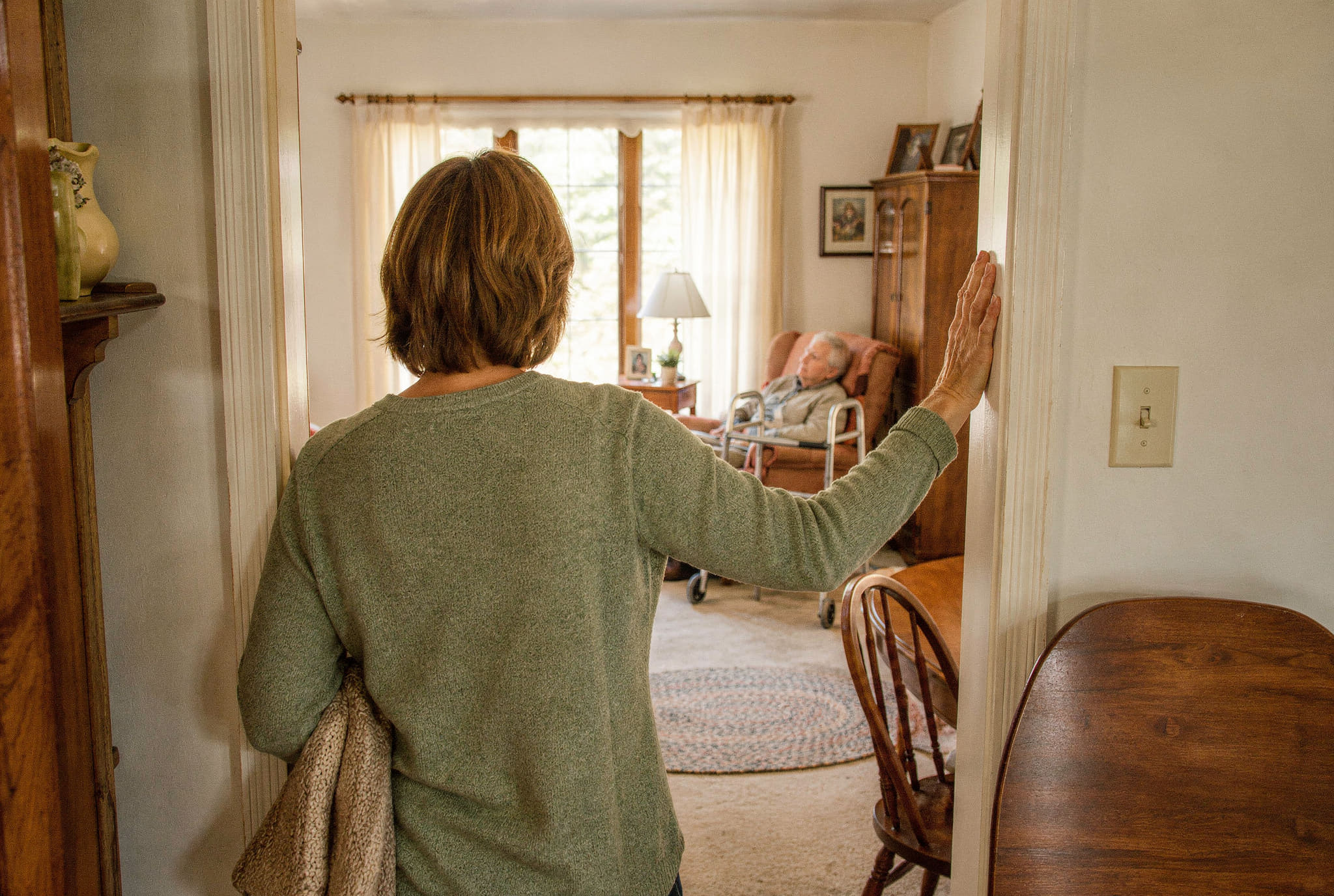 A woman pausing in a doorway, an older relative resting in the next room